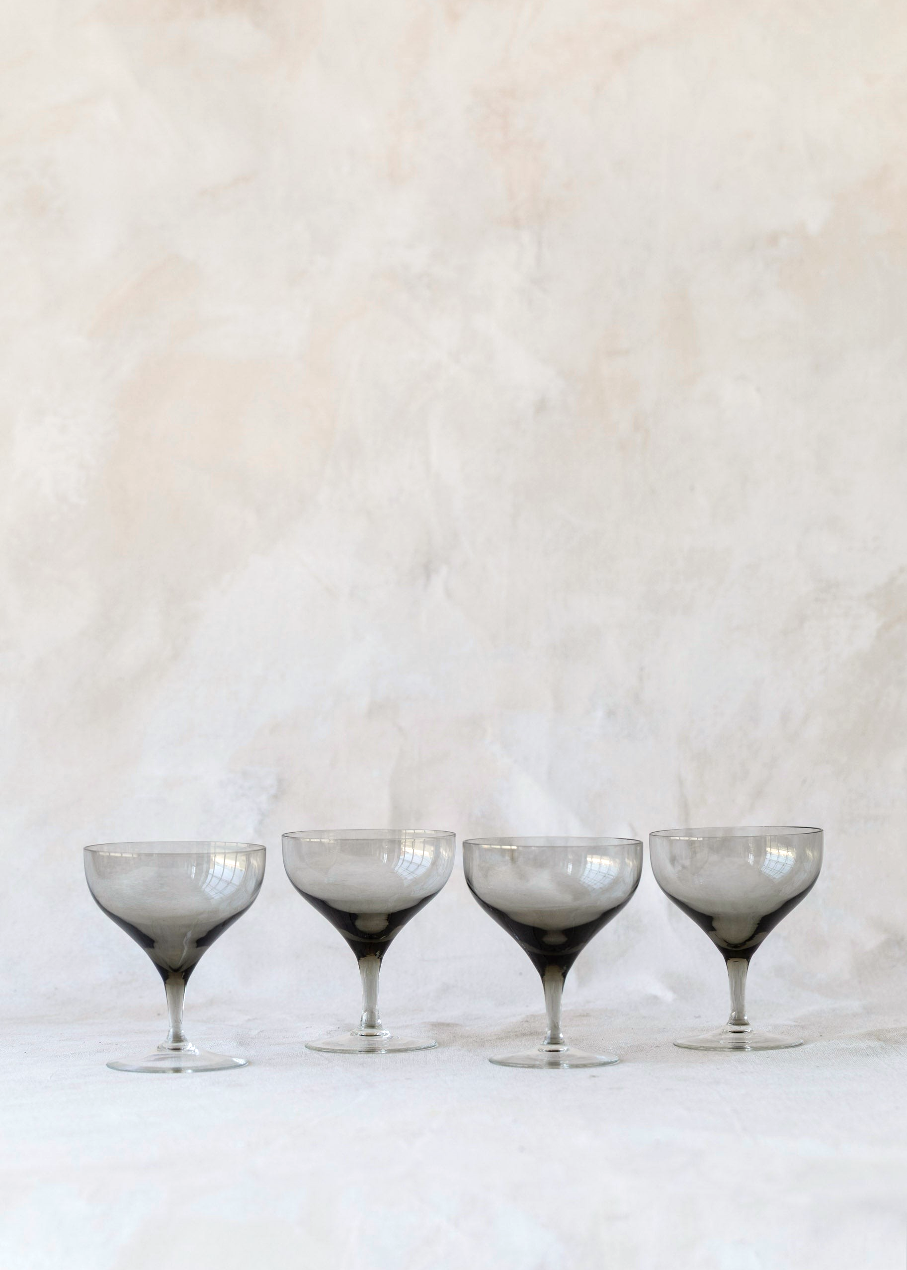 Hoppe Shoppe set of four vintage crystal coupe glasses with smoky charcoal bowls and clear stems on a linen surface.