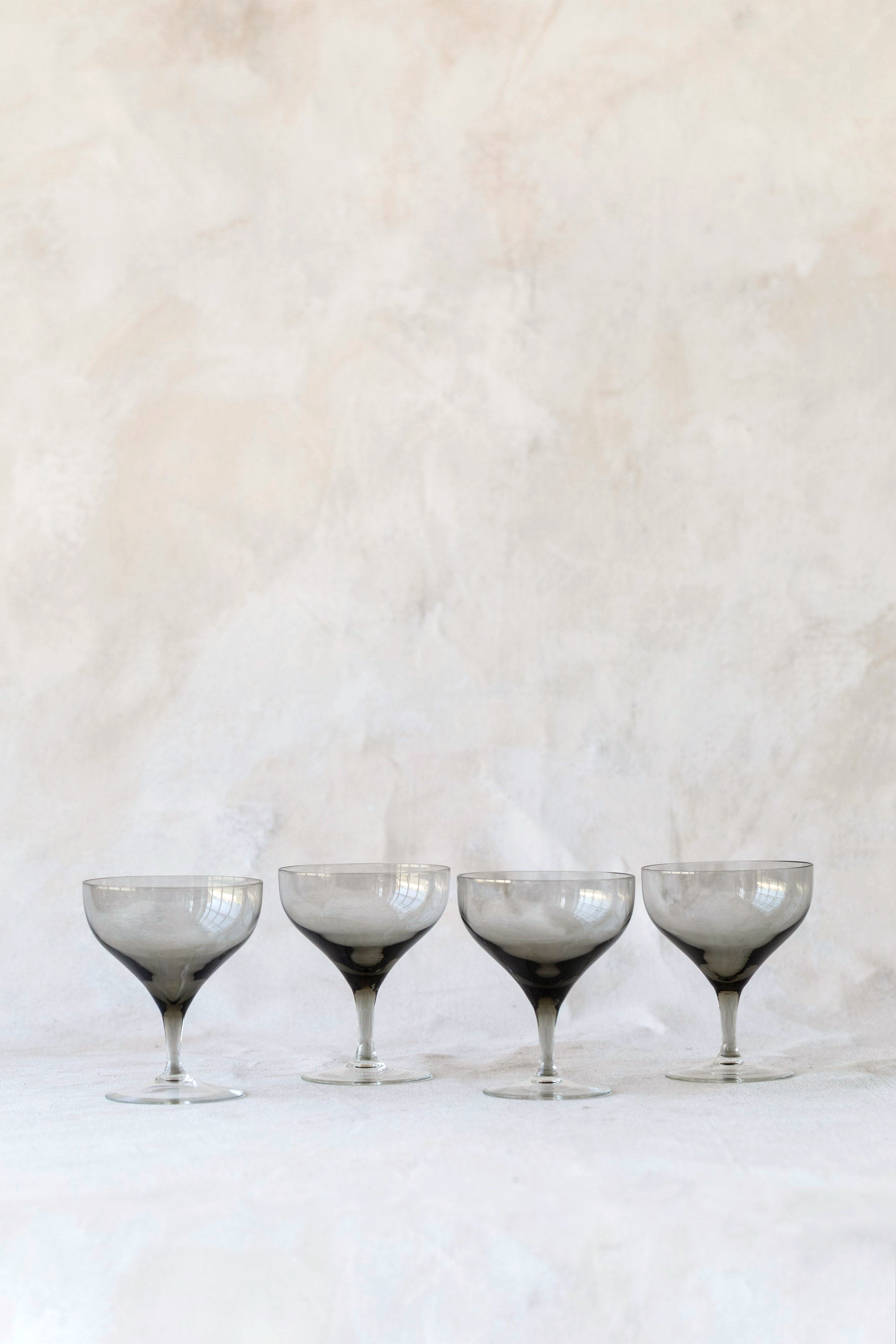 Hoppe Shoppe set of four vintage crystal coupe glasses with smoky charcoal bowls and clear stems on a linen surface.
