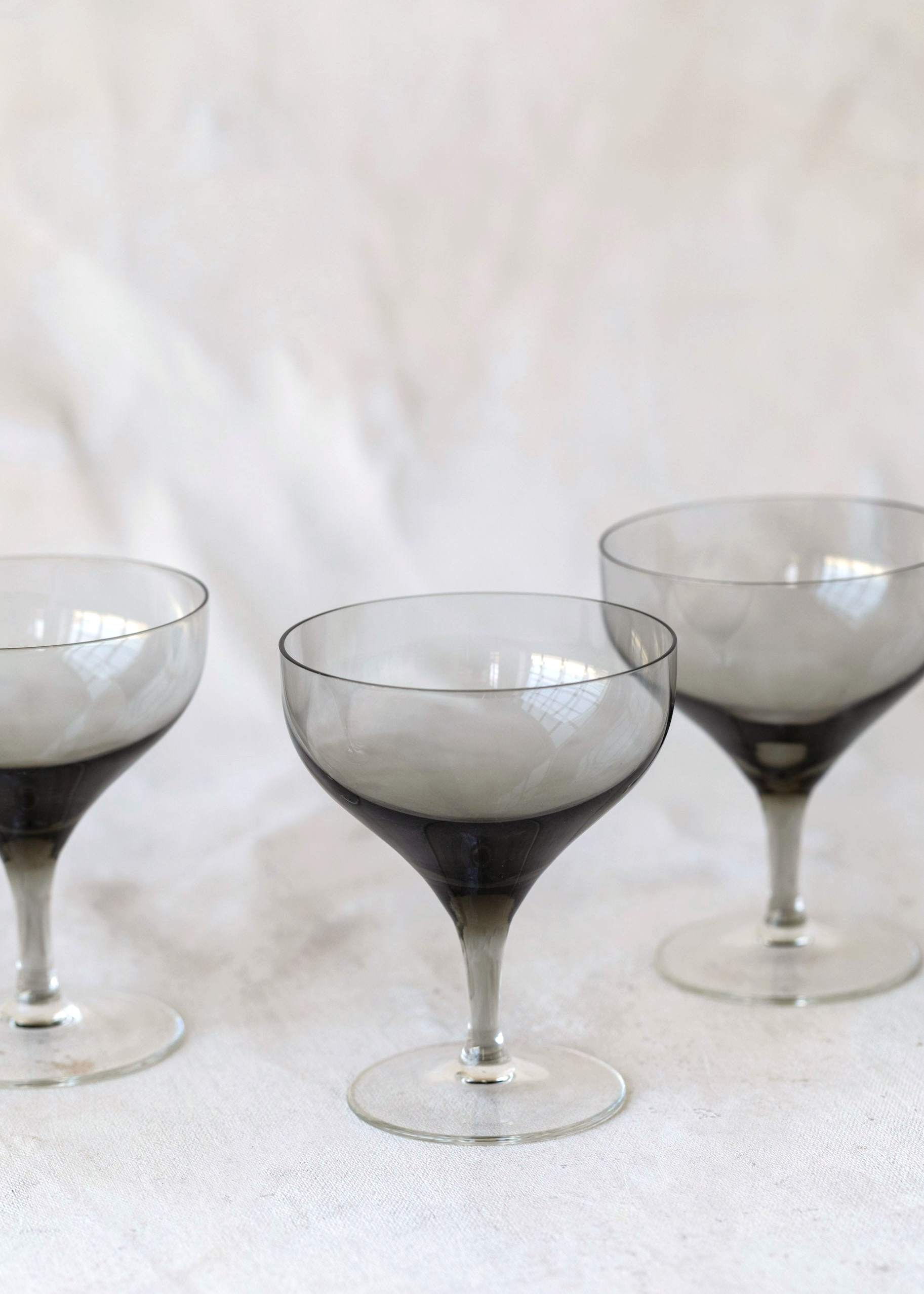 Hoppe Shoppe set of three vintage crystal coupe glasses with smoky charcoal bowls and clear stems on a white cloth.