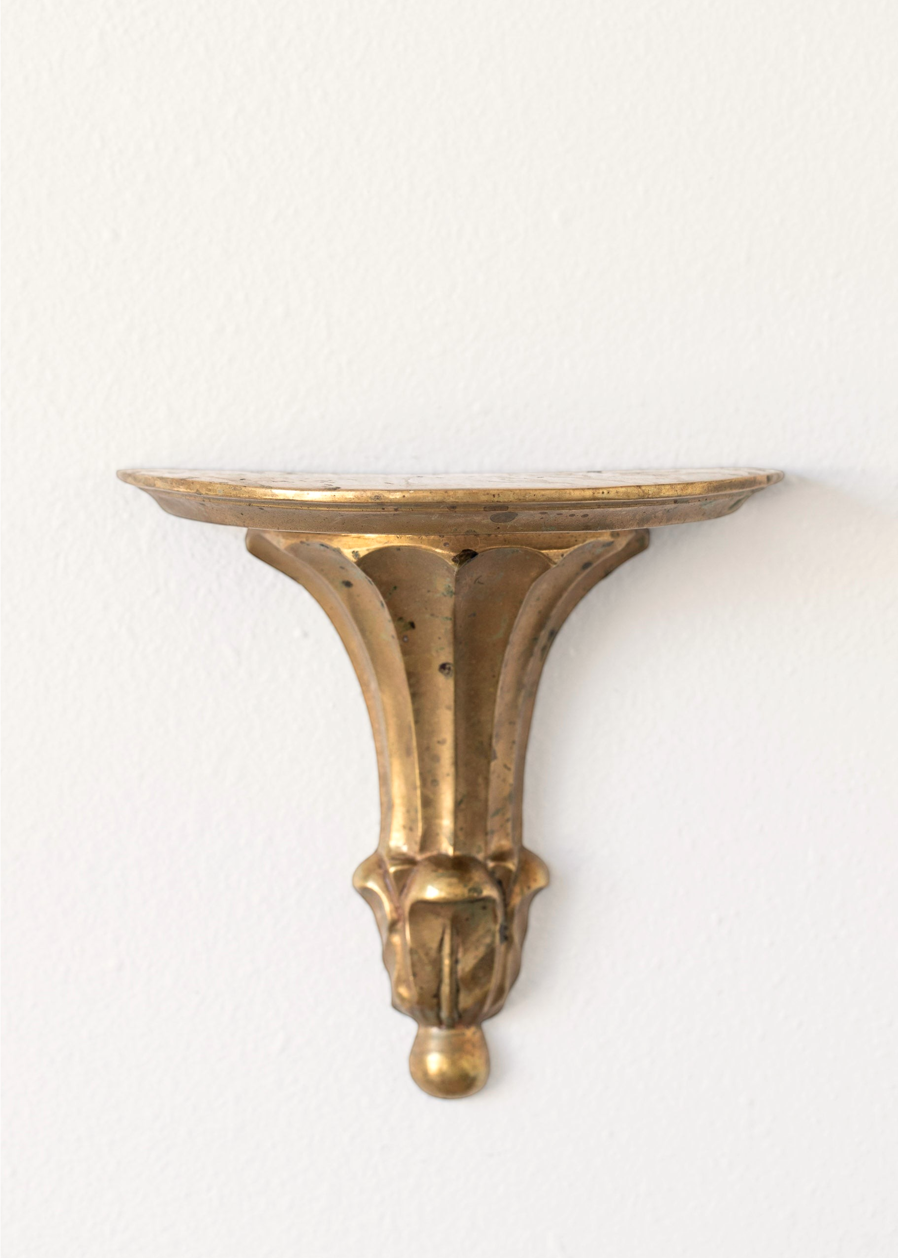 Hoppe Shoppe vintage brass wall shelf with an oval top, ornate fluted corbel, and aged patina on a white wall.