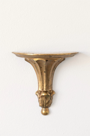 Hoppe Shoppe vintage brass wall shelf with an oval top, ornate fluted corbel, and aged patina on a white wall.
