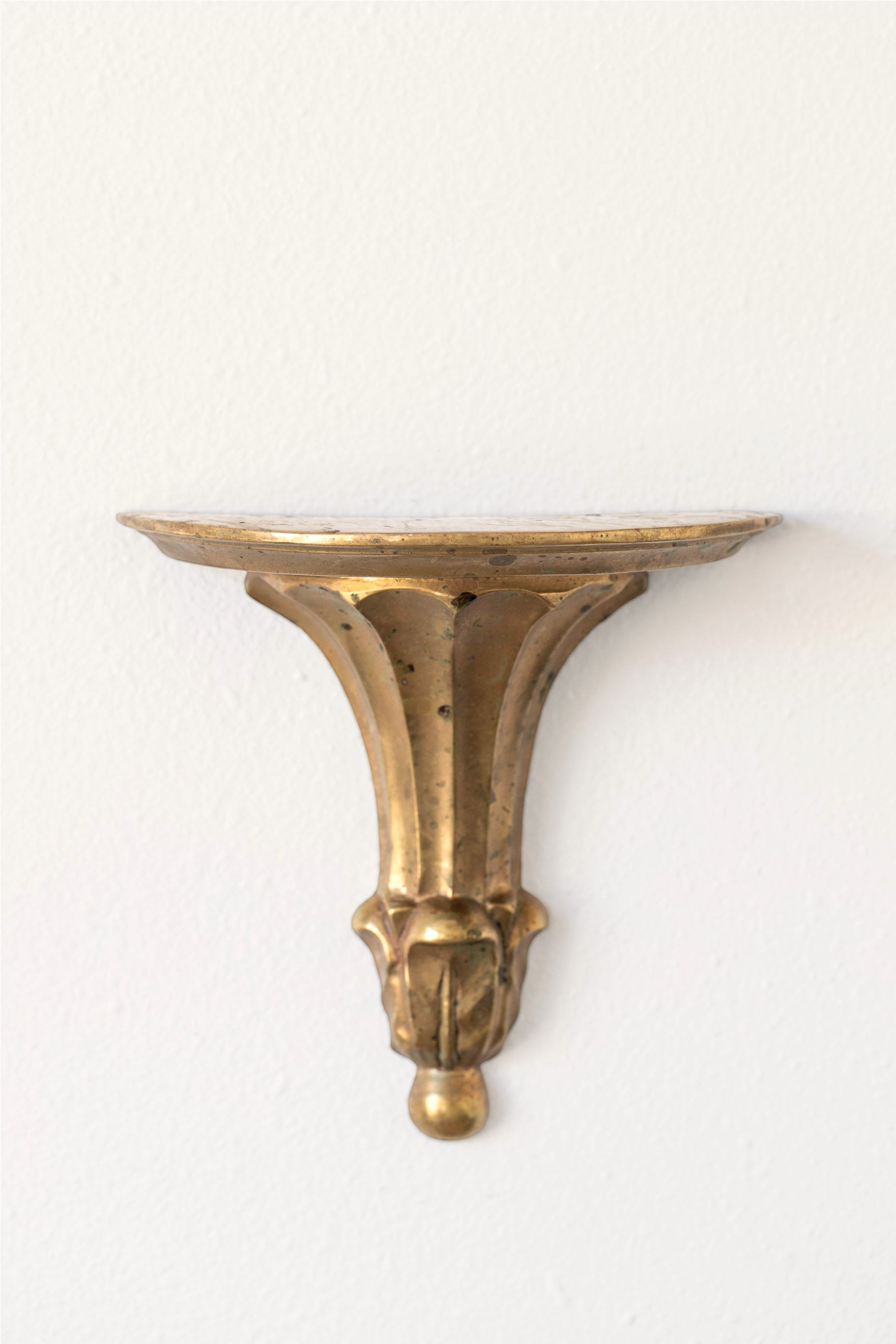 Hoppe Shoppe vintage brass wall shelf with an oval top, ornate fluted corbel, and aged patina on a white wall.